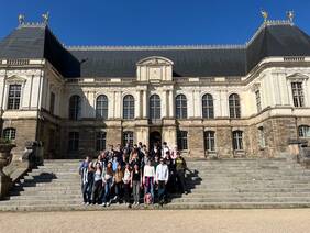 Das Bild zeigt eine große Gruppe von Schülern vor dem Parlament der Bretagne. Die Schüler nehmen an einem Schüleraustausch mit Rennes teil und haben sich für ein Gruppenfoto vor dem imposanten Gebäude versammelt. Der Hintergrund ist sonnig und der Fokus liegt auf den Schülern und dem historischen Gebäude.